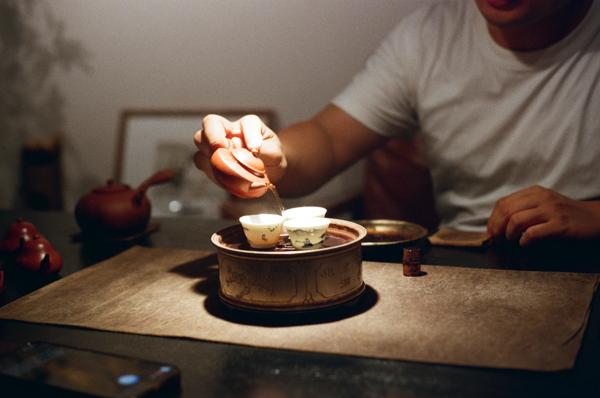 Pouring tea from a small red clay teapot into cups