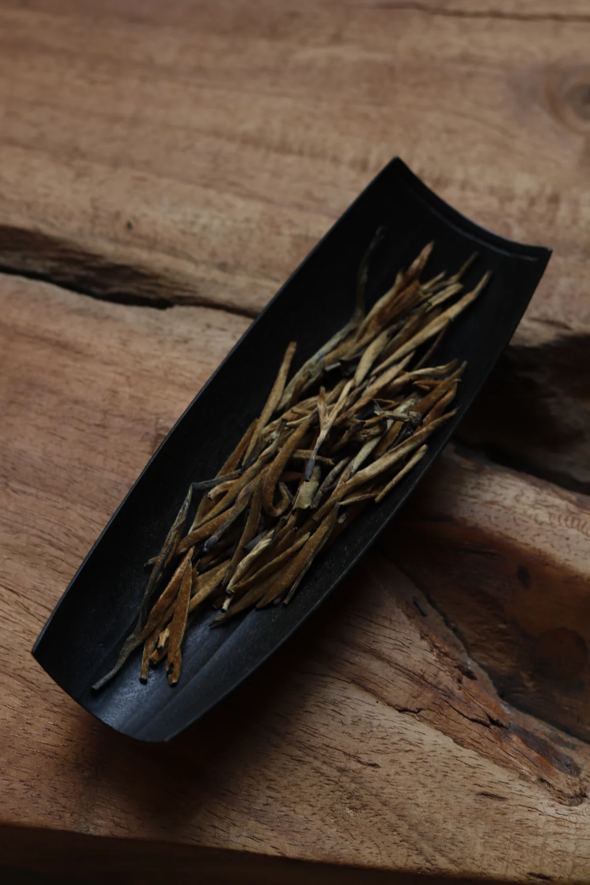 Dianhong Golden Needles tea buds on a dark scoop resting on wood