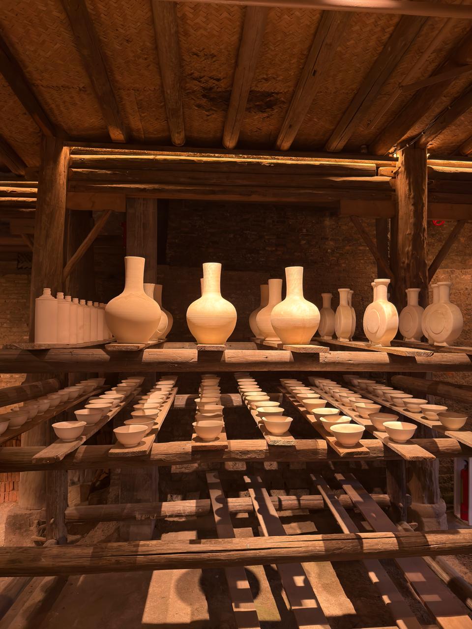 Porcelain vases and bowls on wooden workshop shelves in Jingdezhen