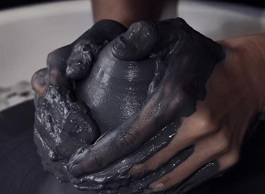 Hands shaping dark clay on a pottery wheel