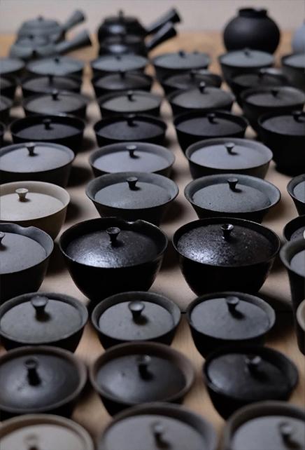 Rows of lidded ceramic vessels in varied dark tones