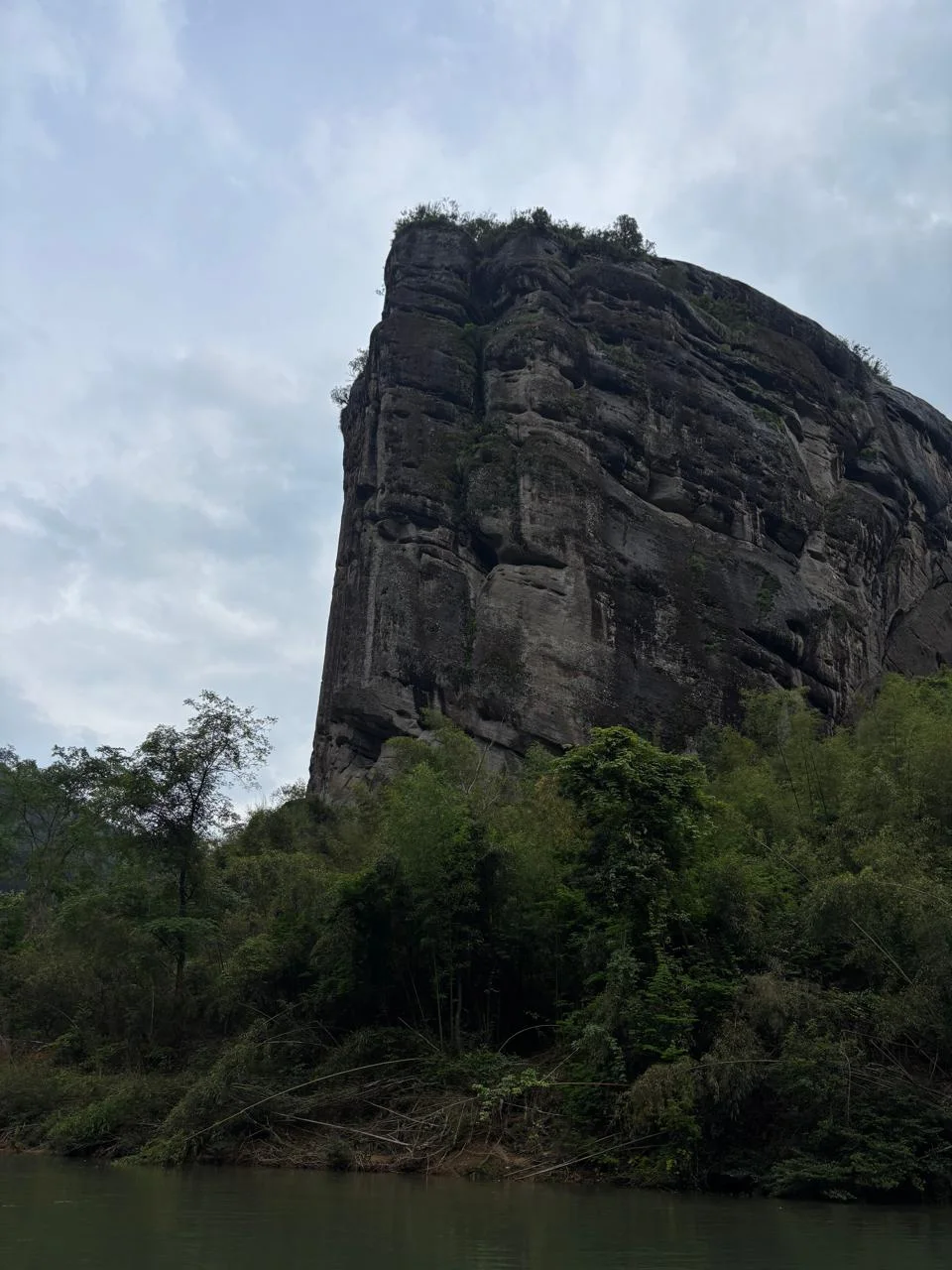 A towering rock cliff above the river and forest in Wuyishan