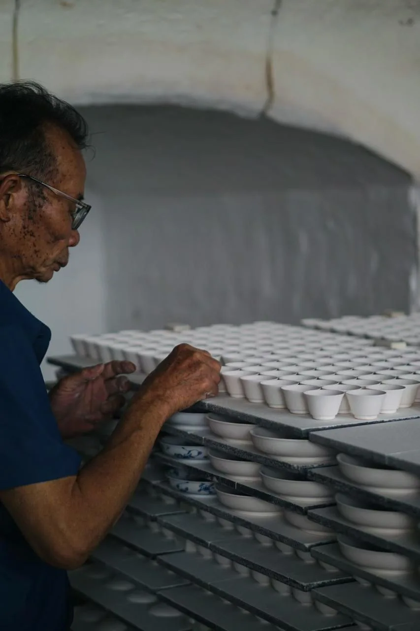 A craftsperson working beside rows of ceramic cups in the studio