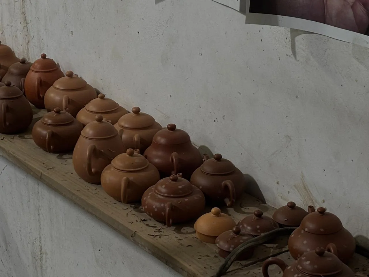 Clay teapots arranged on a wooden shelf in Yujian’s studio