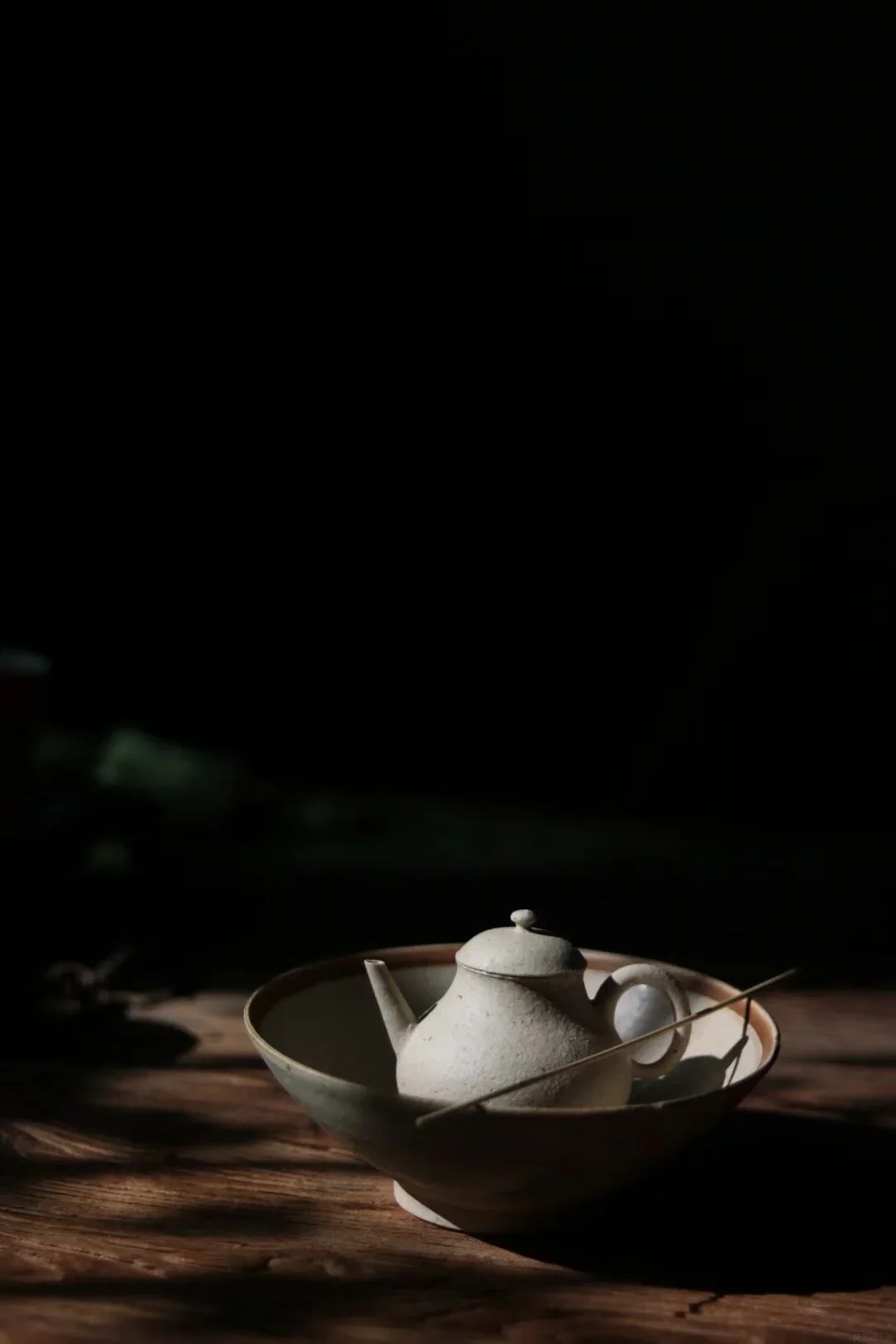 A pale teapot resting in a bowl in subdued light